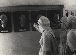 Three women in traditional Yemeni costume study images placed on a wall. 