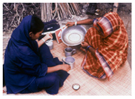 A villager pours water into cup while BRAC teacher looks on