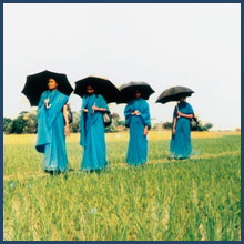 Four BRAC workers with chaperone walk in field.