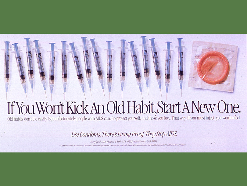 Color photograph of a line of syringes with a condom on the far right