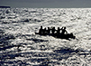 People on a canoe are in the middle of the sea. A small section of the sky can be seen above.