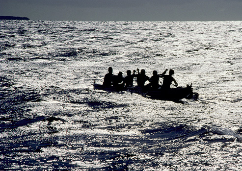 People on a canoe are in the middle of the sea. A small section of the sky can be seen above.