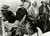 Black and white photograph of a group of 4 elderly people and a younger woman holding a baby sit on a boat headed for Kaho‘olawe.