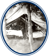 Black and white photograph of the tented hospital Ward 1 at Smoketown Hospitala through the front open end with patients in beds and a female nurse tending to patients. Courtesy Edward G. Miner Library, University of Rochester Medical Center and Robert Zeller.