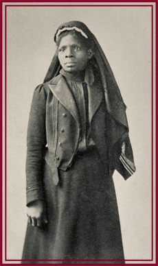 Three-quarters length, standing, full face to left, black and white photograph of Susie King Taylor standing in a uniform wearing a head covering.