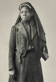 Three-quarters length, standing, full face to left, black and white photograph of Susie King Taylor standing in a uniform wearing a head covering.