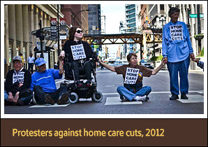 6 White people sit and stand in a street holding hands, one person is in a wheelchair.