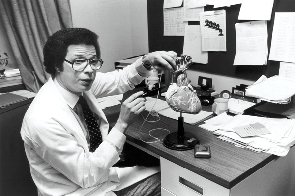 Man seated at a desk with a model of the heart on the desk.