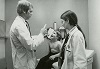 A White woman and man in lab coats examine a smiling White boy sitting on an examination table.