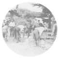 Outdoor view of three men are preparing sprayers to kill ground squirrels. A man in uniform leans against a fence while other men stand watching.