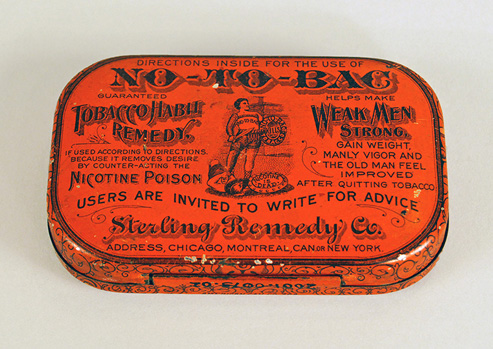 Photograph of the top of an orange anti-tobacco tin with advertisement engraved on it.