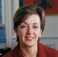 Dr. Jo Ivey Boufford, a White female posing in a red collared jacket. A computer is in the background.