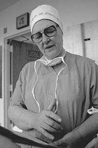 Dr. Benjy Frances Brooks, a White female wearing scrubs, glasses, and a cap looking down at a chart.