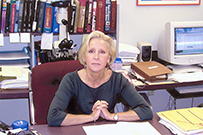 Dr. Mary E. Schmidt Case, a White female seated at her desk in front of a book case, microscope, and computer.