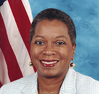 Dr. Donna M. Christian-Christensen, a smiling African American female posing in front of the American flag for her portrait.