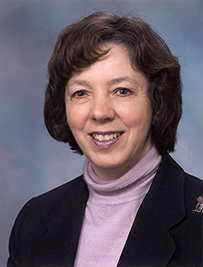 Dr. Judith Salmon Kaur, a White female with short hair in a lilac turtleneck and dark suit posing for her portrait.