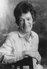 Dr. Jean Baker Miller, a smiling White female posing on a chair for her portrait.