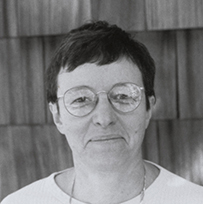 Dr. Lucy M. Candib, a White female wearing glasses posing in front of a shingled structure.