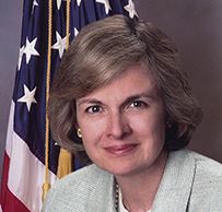 Dr. Eve Elizabeth Slater, a White female in a suit jacket posing in front of the American Flag for her portrait.