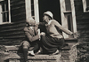 An older man and woman smiling at each other and sitting on stairs in front of a building.