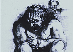 A powerfully built, angry looking man is sitting on the floor, arms folded and knees are drawn up close, his head is turned to the left; his wrists and ankles are in irons which are chained to the wall